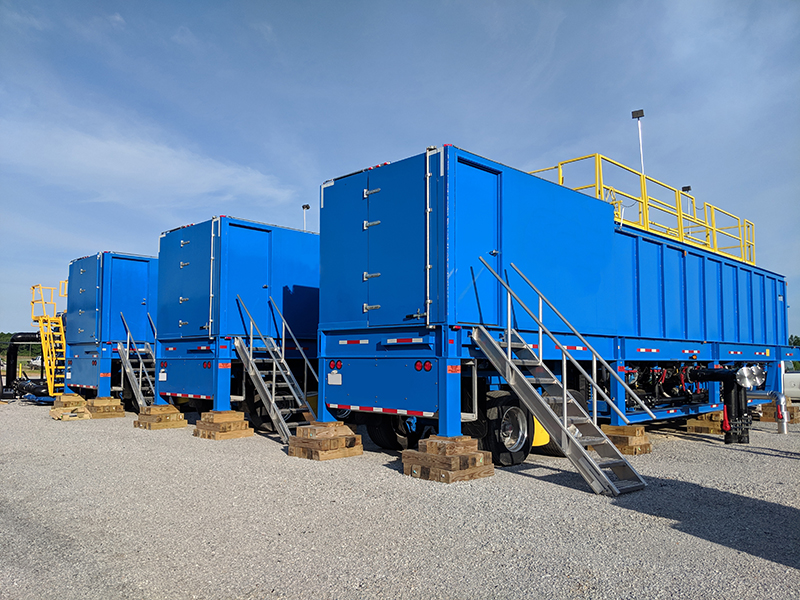 Three blue portable clarifiers lined up in a gravel parking lot.