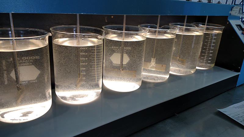 Seis vasos de precipitados de laboratorio de vidrio con líquido transparente en ellos instalados en un sistema de prueba de laboratorio en frascos para el agua.