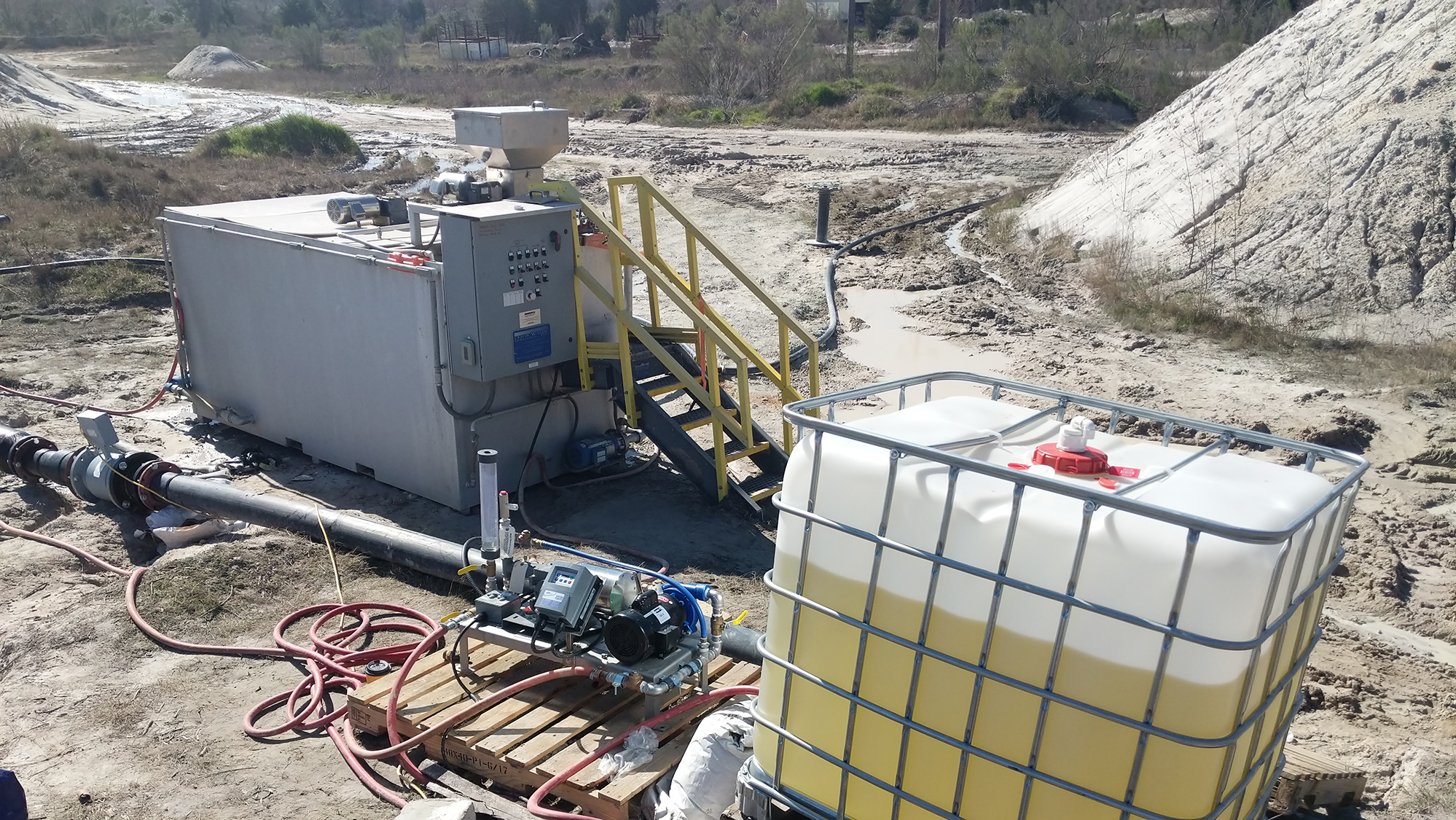 A tote holding unidentified liquid with a liquid polymer skid and a dry polymer preparation system setup in the background at a sand and gravel facility.