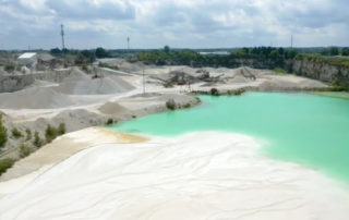 A drone photo of a limestone quarry showing the machines and ground stone in the distance and the settling pond in the foreground.