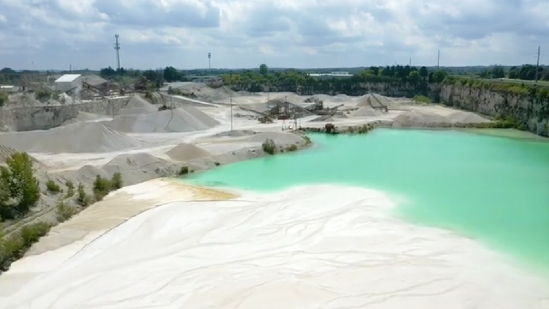 A drone photo of a limestone quarry showing the machines and ground stone in the distance and the settling pond in the foreground.