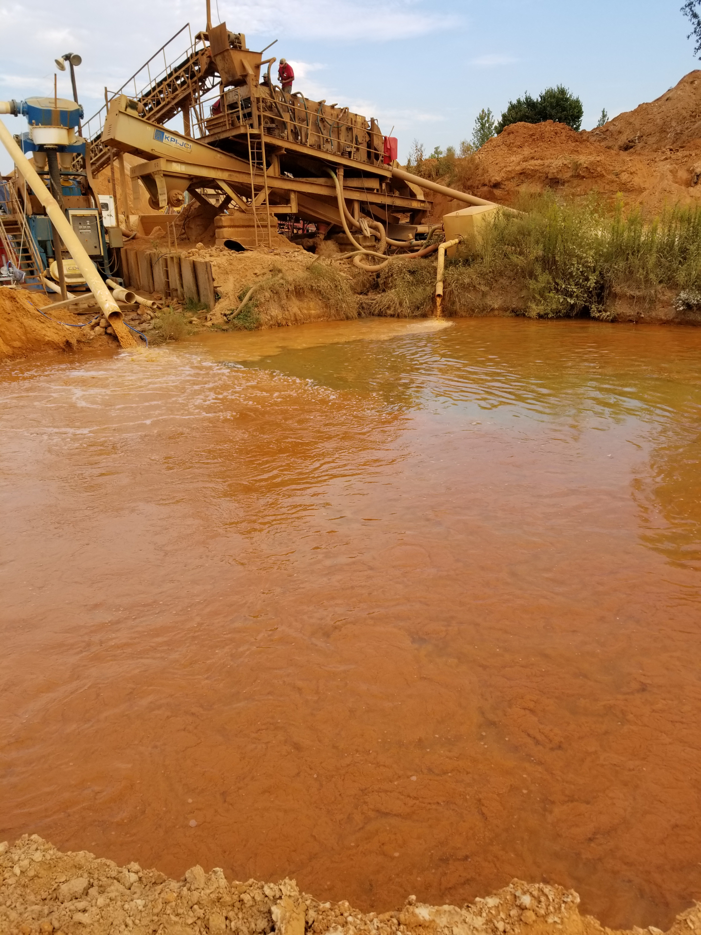 An industrial sand washing plant discharges reddish slurry into a settling pond where the solids are dosed with a polymer solution to create flocculation and sedimentation of the solids.
