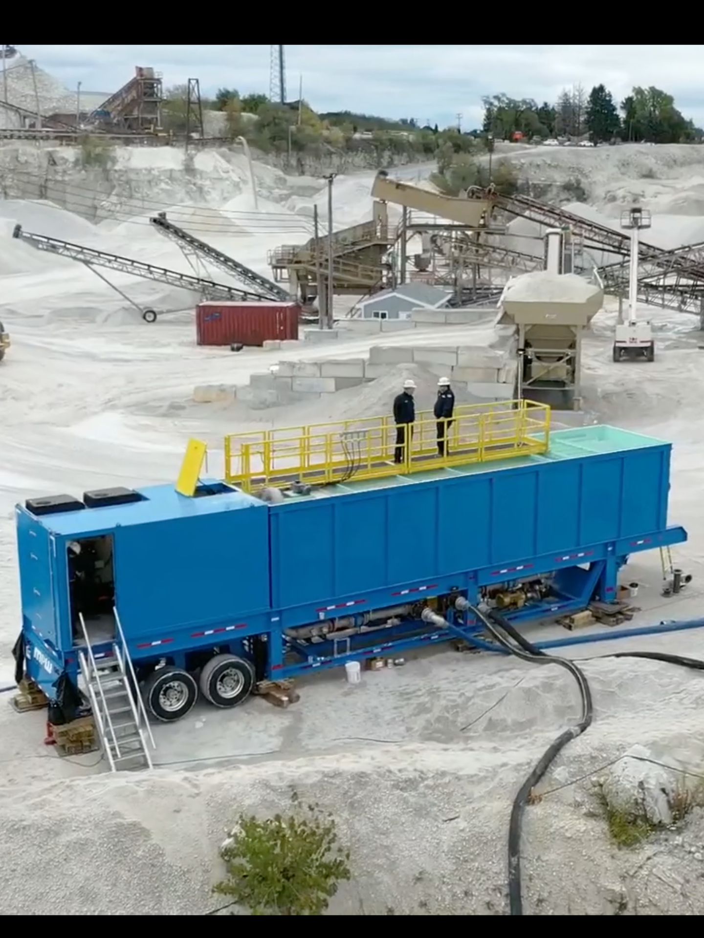 A rectangular portable industrial water clarifier setup at a quarry with two men standing on top of it.