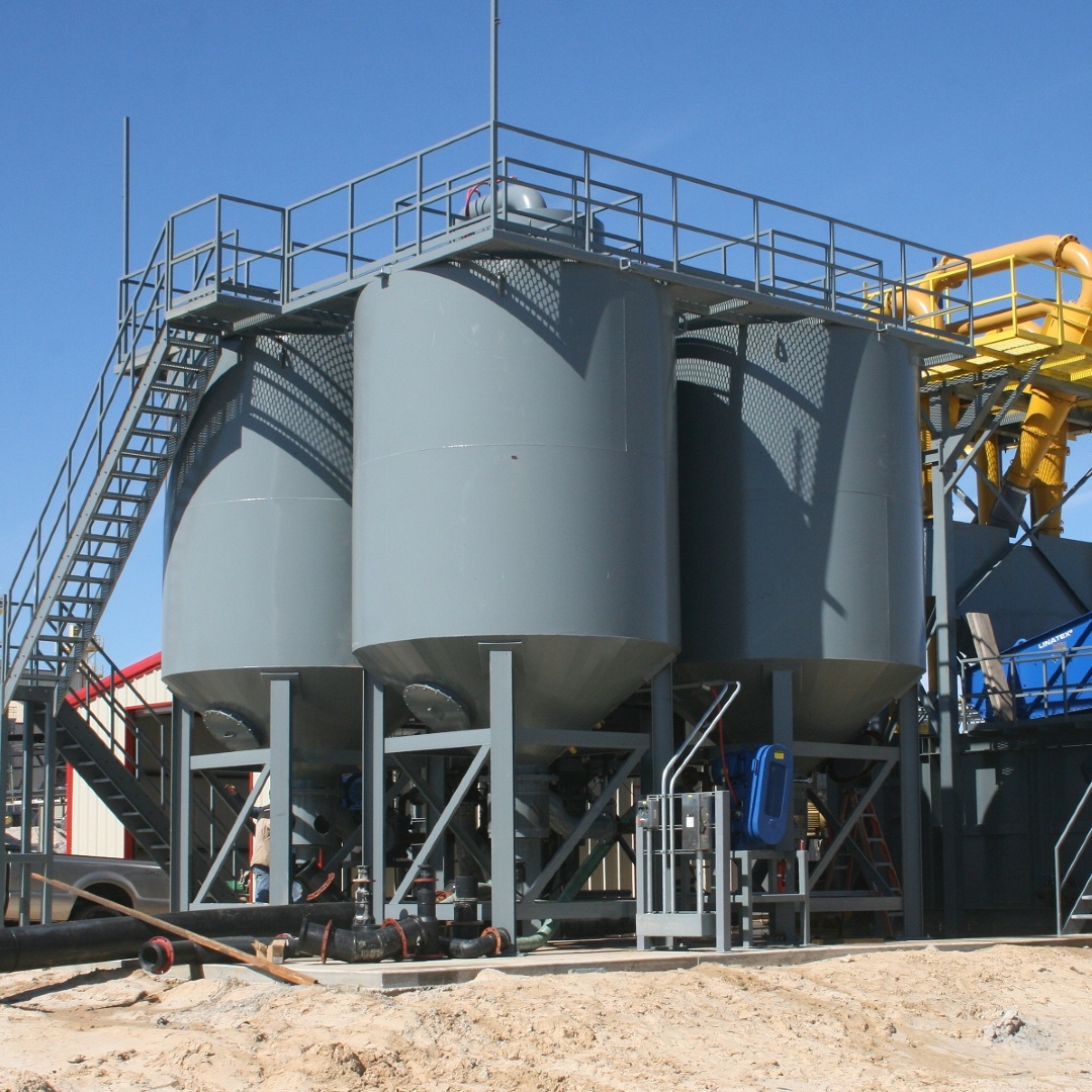 Four grey cone bottom vertical tanks with a catwalk on top of them.