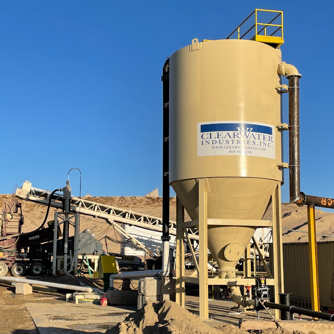 A sun-soaked, cone bottom, clarifier tank in a sand & gravel pit with the Clearwater Industries logo on it.