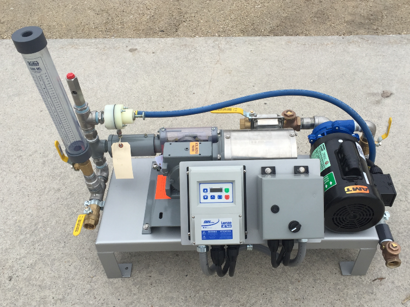 A small chemical feed system with a chemical piston pump, dilution water pump, calibration column, VFD, piping and on/off switch.