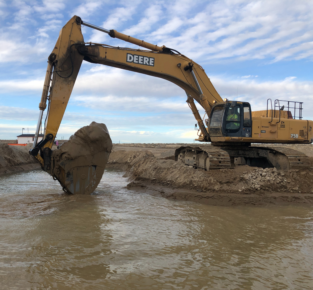 A yellow excavator with a bucket full of mud from a settling pond.