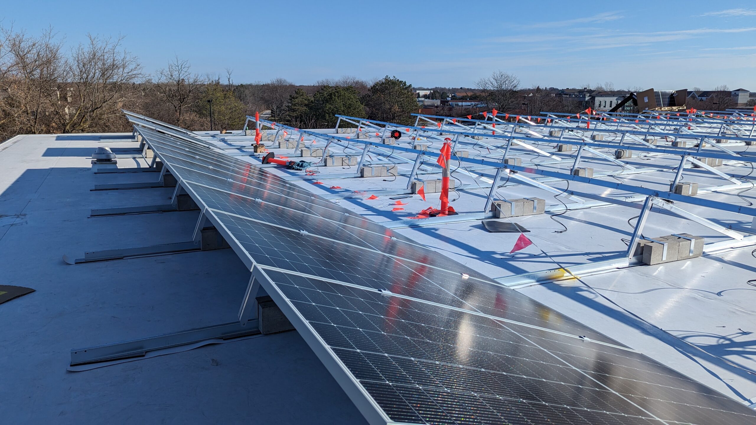 A row of solar panels on top of an industrial building roof with construction flags and more solar panel frames in the background.