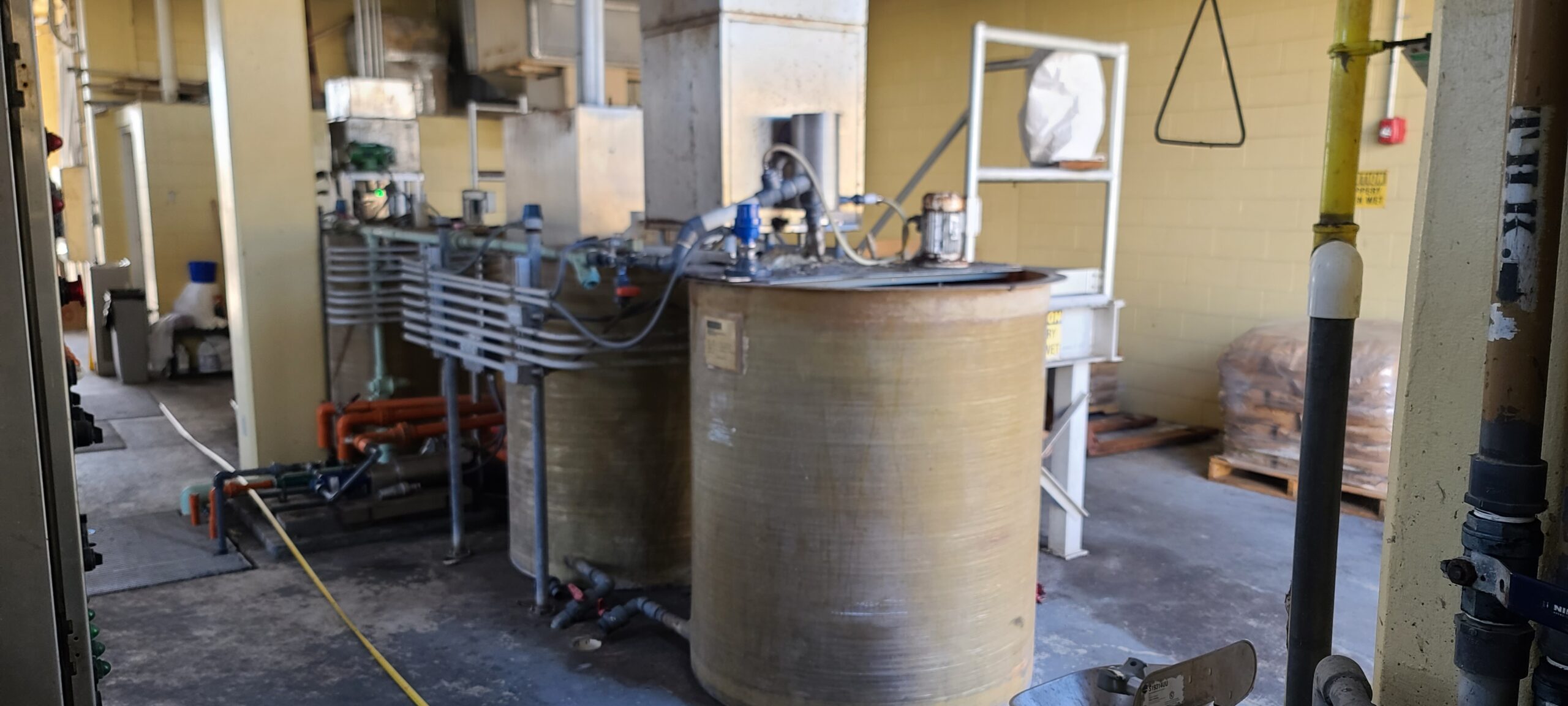Two old round tanks with motorized impellers and outdated industrial steel equipment that create a run down polymer system. The equipment is inside a portion of a wastewater treatment building.