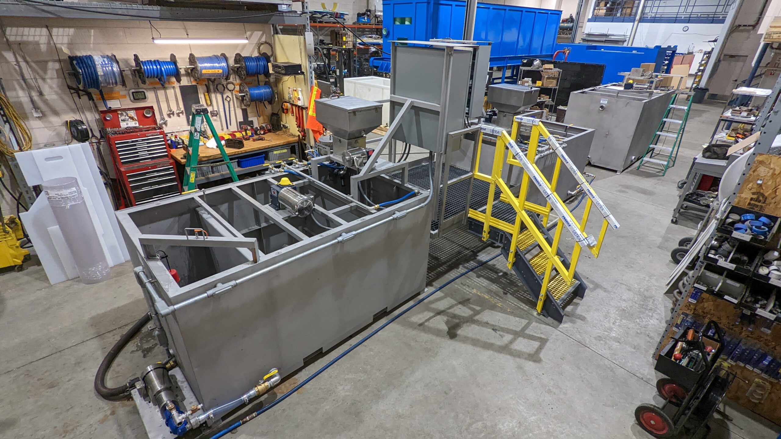 Several rectangular stainless steel tanks with motors and piping inside a manufacturing facility.