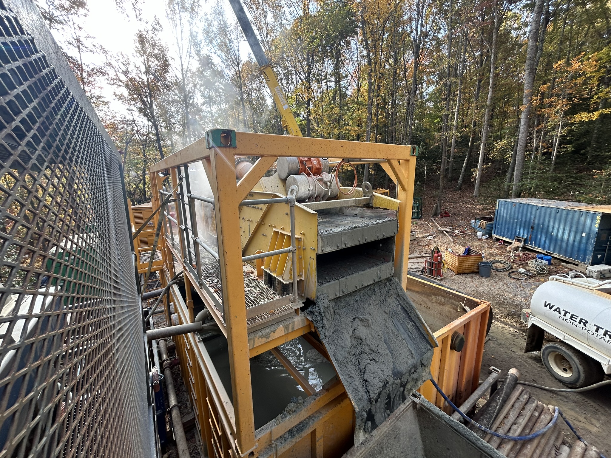 A yellow shaker screen system with mud and solids sliding down its discharge chute.